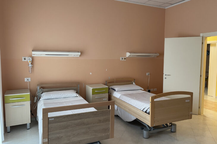 Stanza ospedaliera con due letti regolabili, comodini e pannelli medici a parete